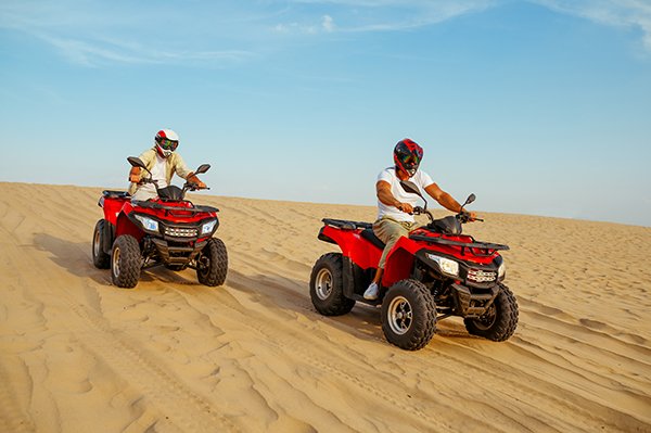 Two racers coming down from the dunes on atv, desert sands. Male persons on quad bikes, sandy race, safari in hot sunny day, 4x4 extreme adventure, quad-biking